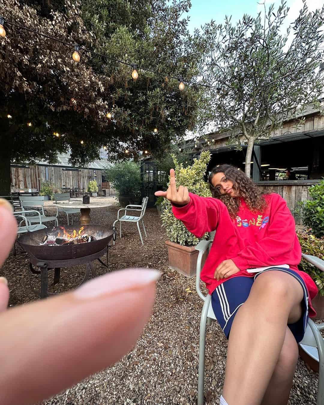 جنا عمرو دياب تجلس على كرسي في حديقة بجانب موقد نار